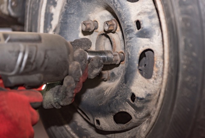 A close up on a tire as a mechanic uses a hydraulic gun to remove the lug nuts and remove the wheel rim.