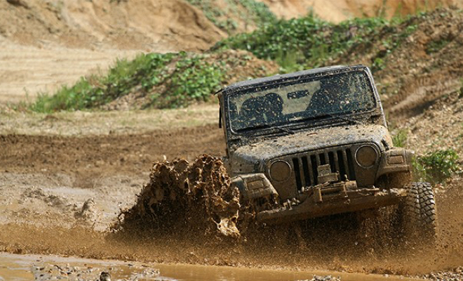 A Jeep driving through a large mud pit