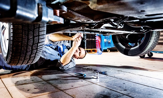 A car lifted at the shop. Mechanic working on suspension of the vehicle under the vehicle