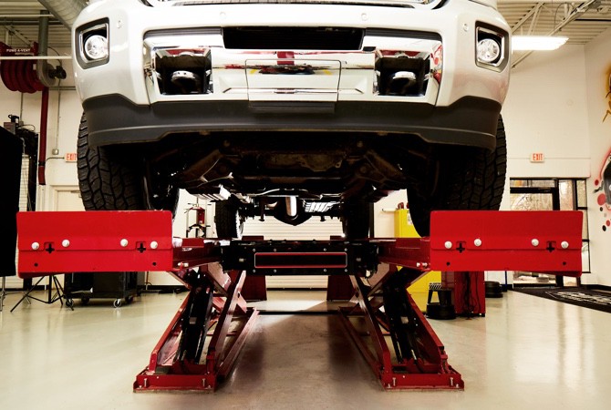 Vehicle-Having-Alignment-Fixed A vehicle that is lifted up into the air on a hoist in a mechanics bay.