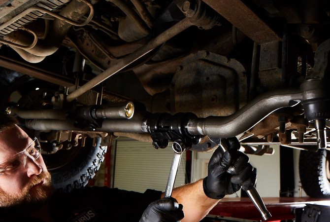 Mechanic-Repairing-Suspension-System A mechanic checking over the bottom of a vehicle to ensure no damage has been done to the undercarriage.