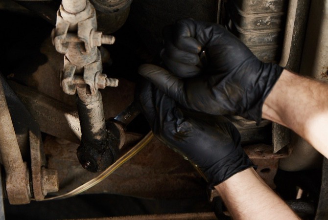 A mechanic's hand adjusting a strut on the bottom of a vehicle.