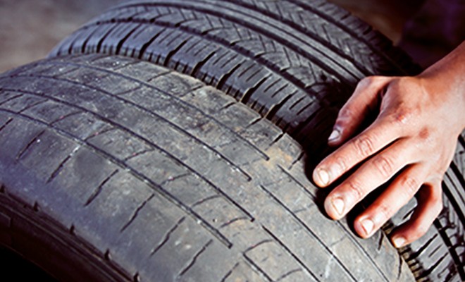 Close up on a tire, specifically tire tread, with a mechanic inspecting it
