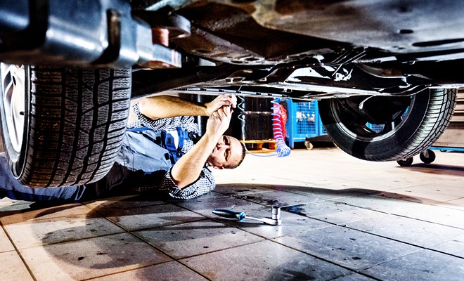 repair-worn-suspension-parts A car lifted at the shop. Mechanic working on suspension of the vehicle under the vehicle